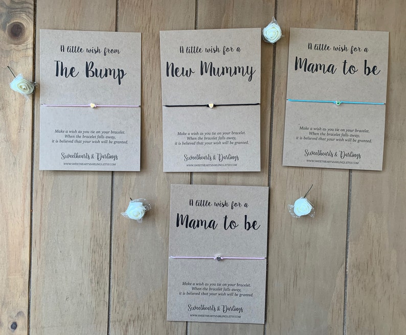 May include: Four cards with a wish bracelet attached to each. The cards are brown and have white text. The text on the cards reads "A little wish from The Bump", "A little wish for a New Mummy", "A little wish for a Mama to be", and "A little wish for a Mama to be".