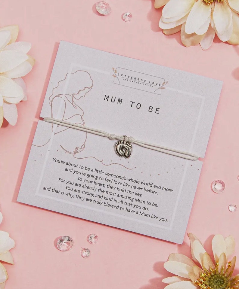 May include: White string bracelet with a silver charm of two tiny footprints. The bracelet is on a white card with the text "Letterbox Love" and "Mum to Be". The card has a line drawing of a pregnant woman.