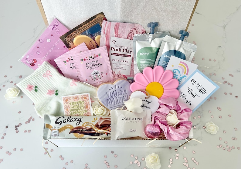 K&ouml;nnte beinhalten: Eine Geschenkbox mit Pflegeprodukten. Enth&auml;lt rosa Gesichtsmasken, Teebeutel, eine Galaxy-Schokoriegel, einen bl&uuml;tenf&ouml;rmigen Keks, einen schwammf&ouml;rmigen Schwamm und eine Karte mit der Aufschrift "A Little Treat for you."