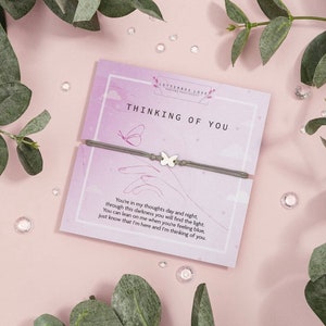 May include: A gray bracelet with a silver butterfly charm and a card that reads "Thinking of You" with a message about being there for someone when they are feeling blue.