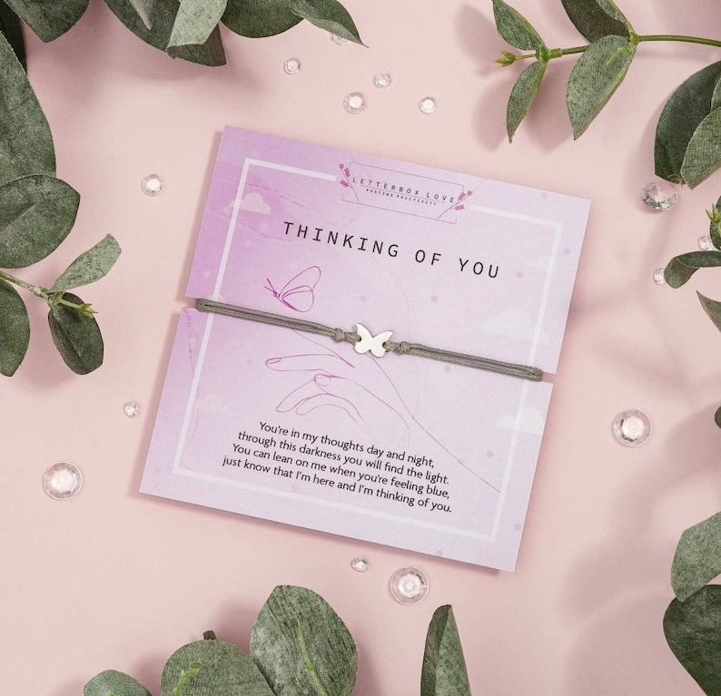 May include: A gray bracelet with a silver butterfly charm and a card that reads "Thinking of You" with a message about being there for someone when they are feeling blue.