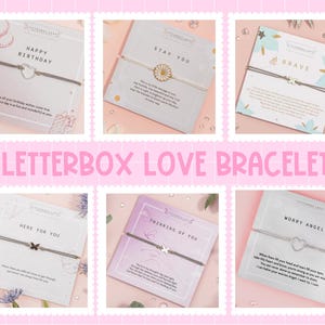 K&ouml;nnte beinhalten: Eine Sammlung von Letterbox Love Armb&auml;ndern, jeweils auf einer Karte mit einer anderen Botschaft. Die Armb&auml;nder haben eine d&uuml;nne Kordel und einen kleinen Anh&auml;nger. Botschaften sind "Happy Birthday", "Stay You" und "Brave".