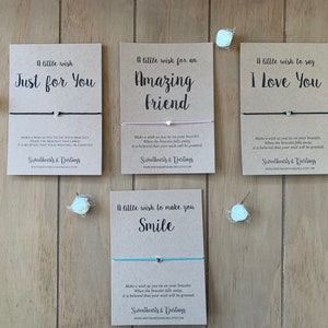May include: Four cards with brown paper backgrounds and black text. Each card has a different message: "A little wish Just for You", "A little wish for an Amazing Friend", "A little wish to say I Love You", and "A little wish to make you Smile". Each card has a string bracelet attached with a small heart charm.