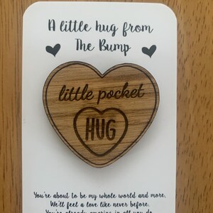 May include: A wooden heart-shaped pocket hug with the word "HUG" inside. The hug is on a white card with the text "A little hug from The Bump" and a message about love and appreciation for a mother.