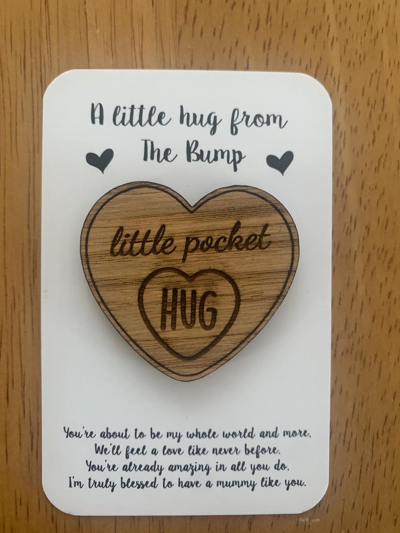 May include: A wooden heart-shaped pocket hug with the word "HUG" inside. The hug is on a white card with the text "A little hug from The Bump" and a message about love and appreciation for a mother.