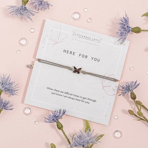 May include: A gray string bracelet with a small butterfly charm. The bracelet is on a white card with the text "HERE FOR YOU" and a message about being there for someone during difficult times.