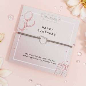 K&ouml;nnte beinhalten: Ein graues Armband aus Schnur mit einem silbernen Herz-Anh&auml;nger und einer Karte mit der Aufschrift "Happy Birthday" mit rosa und wei&szlig;en Ballons und Sternen. Die Karte sagt auch "M&ouml;gen all deine Geburtstagsw&uuml;nsche in Erf&uuml;llung gehen und dein Tag so lustig und wunderbar sein wie du."