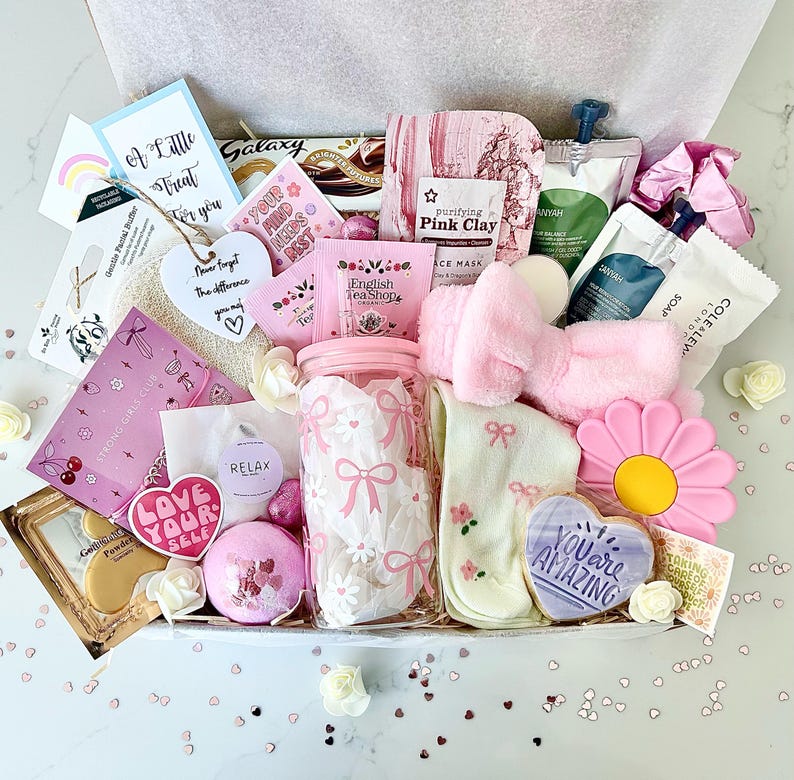 K&ouml;nnte beinhalten: Eine Geschenkbox mit Selbstpflegeartikeln in Rosa, darunter ein Glas mit Schleifen, Gesichtsmasken, ein Stirnband, Socken und ein herzf&ouml;rmiger Keks mit der Aufschrift "You are Amazing".