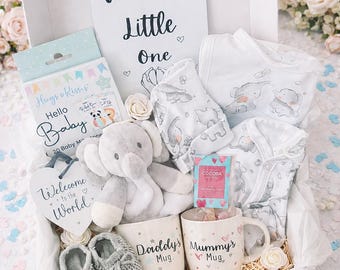 Puede incluir: Una caja de regalo blanca que contiene una tarjeta Welcome Little One, un elefante de peluche gris, dos tazas blancas con las etiquetas Daddy's Mug y Mummy's Mug, patucos de punto grises, ropa de bebé con estampado de elefantes y tarjetas Hello Baby.