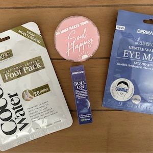 May include: A collection of self-care products, including a foot pack, eye mask, lavender roll-on, and a pink circular decorative item with the text "Do what makes your soul happy". The foot pack is labeled "Coconut Water".