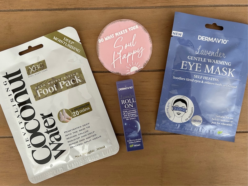 May include: A collection of self-care products, including a foot pack, eye mask, lavender roll-on, and a pink circular decorative item with the text "Do what makes your soul happy". The foot pack is labeled "Coconut Water".