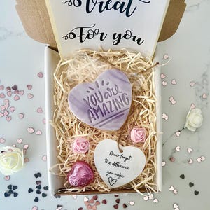 K&ouml;nnte beinhalten: Eine Geschenkbox mit einem herzf&ouml;rmigen Leckerli mit der Aufschrift "You Are Amazing". Die Box enth&auml;lt Dekopapier, rosa Rosen, eine herzf&ouml;rmige Schokolade und ein Herz-Tag mit der Aufschrift "Never forget the difference you make."
