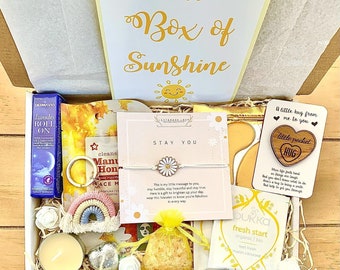 May include: A yellow gift box filled with various self-care items, including a small candle, a daisy bracelet, a wooden heart with the words "little pocket hug", a small bag of bath salts, and a card that says "Stay You".