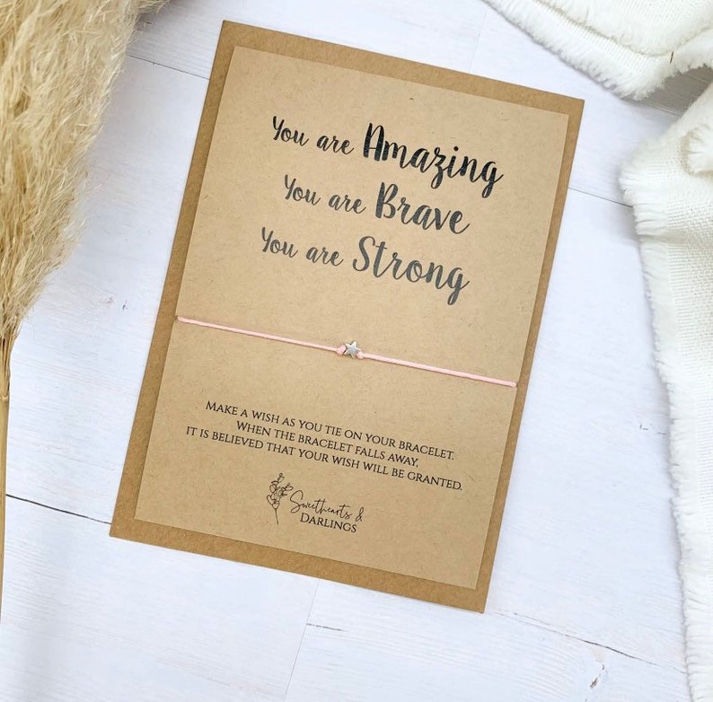 May include: A pink and silver wish bracelet with a star charm. The card reads "You are Amazing, You are Brave, You are Strong. Make a wish as you tie on your bracelet. When the bracelet falls away, it is believed that your wish will be granted. Sweethearts & Darlings."