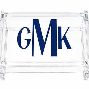 May include: A clear acrylic rectangular tray featuring a dark blue monogram with the letters GMK printed in the center. The tray has a transparent, rigid structure with raised edges and a smooth, polished finish on all visible surfaces.