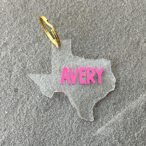 May include: A clear acrylic keychain shaped like the state of Texas with the name "AVERY" printed in pink.