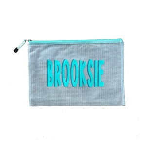 May include: A clear mesh zippered pouch with a turquoise zipper and the name "BROOKSIE" printed in turquoise.
