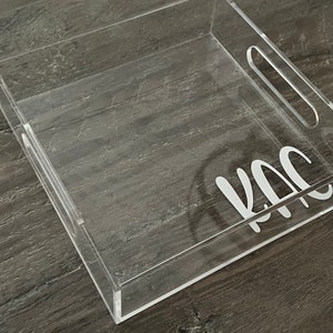 May include: A clear acrylic tray with a handle and the word "KAC" written on the bottom.