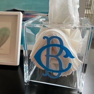 May include: A clear acrylic tissue box cover with a blue monogram "BC" on the front. The tissue box is filled with white tissues.