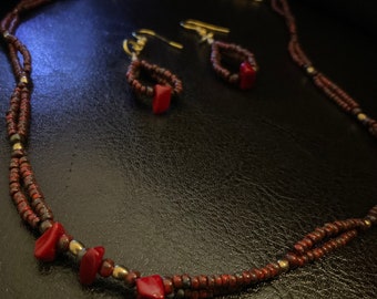 May include: A red and gold beaded necklace and matching earrings. The necklace is made of two strands of small beads, one red and one gold. The earrings are simple, with a single red bead hanging from a gold hook.