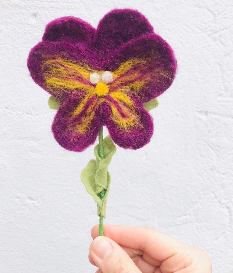 May include: A purple felt flower with a yellow butterfly design and green felt leaves on a stem.