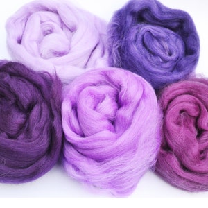 Puede incluir: Cinco ovillos de lana en tonos de morado, lavanda y rosa. La lana es suave y esponjosa, perfecta para tejer o hacer ganchillo.