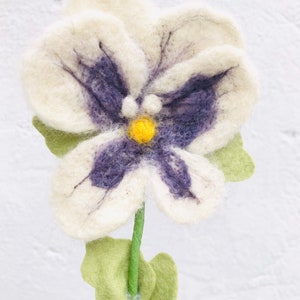 May include: A white felt flower with purple and yellow accents. The flower has a stem and green leaves.