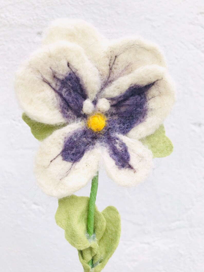 May include: A white felt flower with purple and yellow accents. The flower has a stem and green leaves.