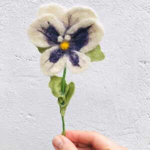 May include: A white felt flower with purple and yellow accents. The flower is hand-crafted and has a green stem.