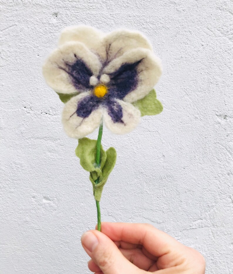 May include: A white felt flower with purple and yellow accents. The flower is hand-crafted and has a green stem.