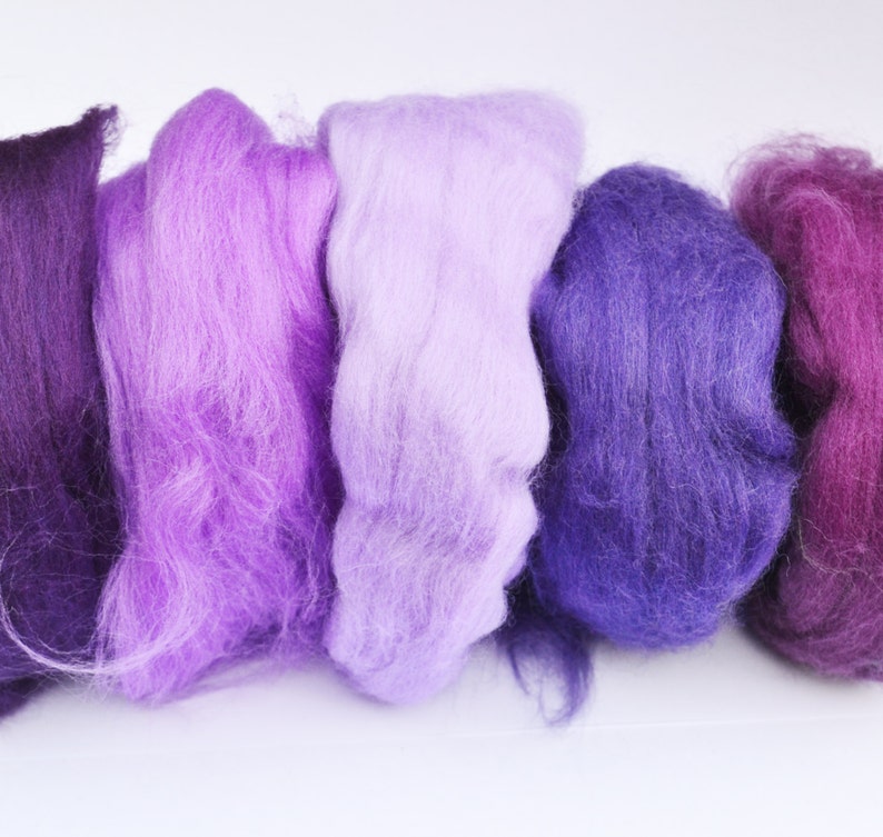 Puede incluir: Cinco madejas de lana cardada en tonos de morado, lavanda y rosa. La lana es suave y esponjosa, perfecta para fieltro o hilado.