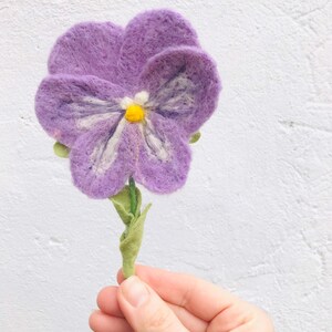 May include: A purple felt flower with a white and yellow center. The flower is on a green stem with leaves.