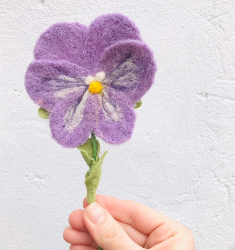 May include: A purple felt flower with a white and yellow center. The flower is on a green stem with leaves.
