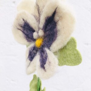 May include: A white felt flower with purple and yellow accents. The flower has a green felt stem and leaves.
