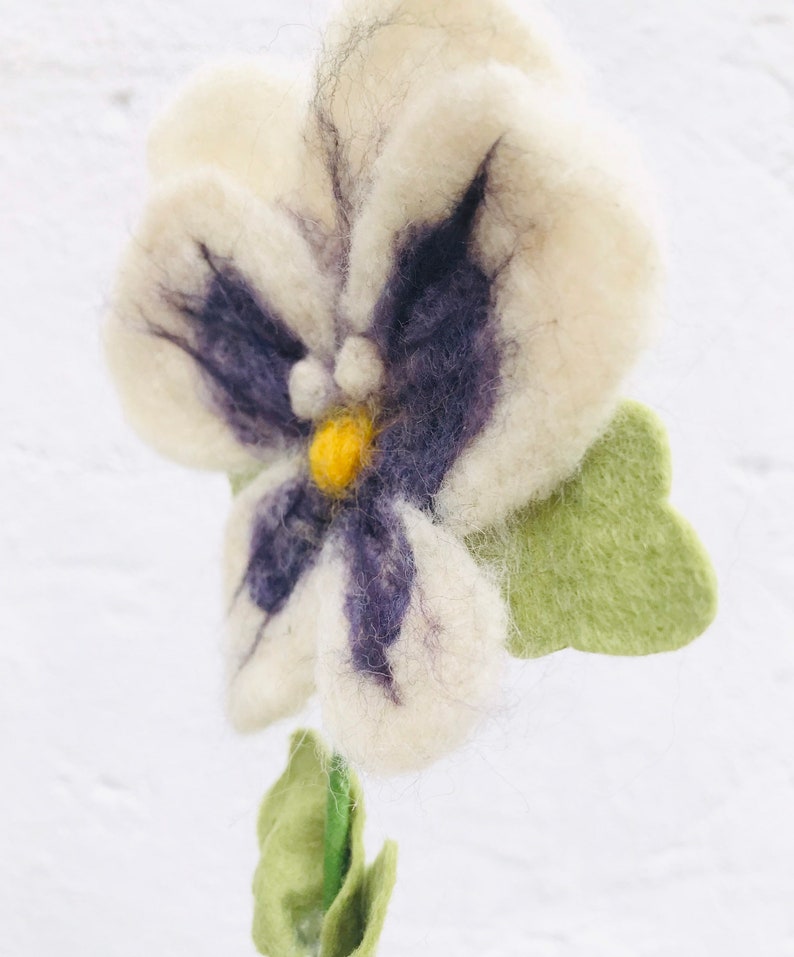May include: A white felt flower with purple and yellow accents. The flower has a green felt stem and leaves.
