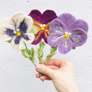 May include: Three felt pansies in white, purple, and burgundy with yellow centers. The flowers are attached to green stems.