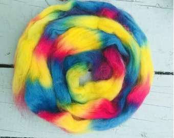 Puede incluir: Primer plano de un hilo de lana de color arcoíris, con tonos de azul, amarillo, rojo y rosa. El hilo está dispuesto en forma circular, creando un patrón de espiral.