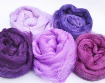 Puede incluir: Cinco ovillos de lana en tonos de morado, lavanda y rosa. La lana es suave y esponjosa, perfecta para tejer o hacer ganchillo.