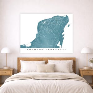 May include: A teal and white map of the Yucatan Peninsula, with roads and cities marked in white. The text "YUCATAN PENINSULA" is printed in white at the bottom of the map. The map is displayed above a bed with white bedding and wooden nightstands.