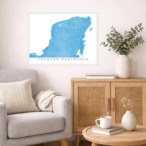 May include: A framed print of the Yucatan Peninsula in a light blue watercolor style. The map shows roads and cities in white against a blue background. The words "YUCATAN PENINSULA" are printed in black at the bottom.