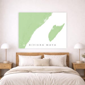 May include: A framed wall art print featuring a map of Riviera Maya in a light green hue against a white background. The text "RIVIERA MAYA" is printed in black. The artwork is displayed above a bed with wooden nightstands and lamps.