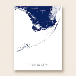 May include: A minimalist art print featuring a detailed map of the Florida Keys in a deep navy blue against a clean white background. The words "FLORIDA KEYS" are printed in a simple, modern font at the bottom of the print.