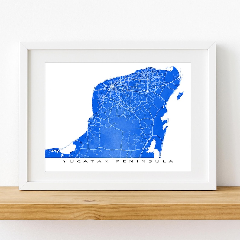 May include: A framed print featuring a blue watercolor map of the Yucatan Peninsula. White lines depict roads and cities. The words "YUCATAN PENINSULA" are printed in a simple font at the bottom of the image.
