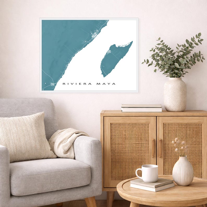 May include: A framed wall art print featuring a teal map of the Riviera Maya coastline. The print has white text that reads "RIVIERA MAYA". The artwork is displayed above a gray armchair and a wooden cabinet with a vase of greenery.