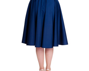 May include: A navy blue, knee-length skirt with a full, flared silhouette. The skirt features a high waist and a zipper closure at the back. The model is wearing white heels. The skirt is made of a solid, opaque fabric.