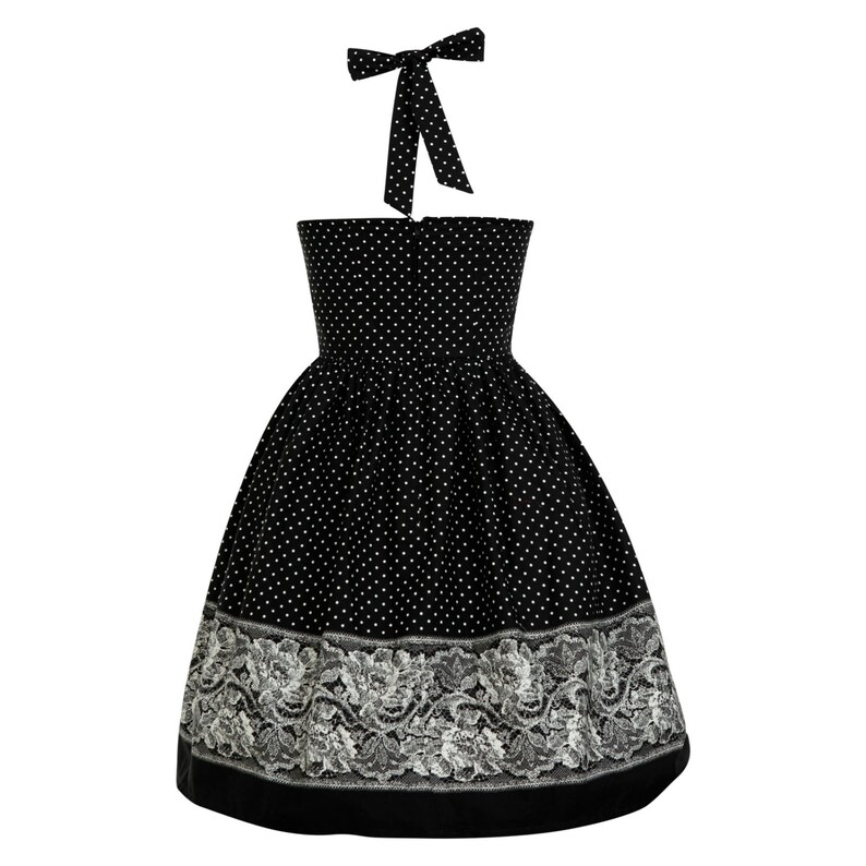 May include: A black halter dress featuring a white polka dot pattern on the bodice and skirt. The hem is decorated with a wide, intricate white floral lace border. The dress includes a matching black and white polka dot tie at the neck.