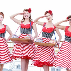May include: Four women in vintage-style dresses with red and white striped skirts, black polka dot bodices, and red tops. They are holding trays of popcorn and saluting. The image has a retro, patriotic theme.