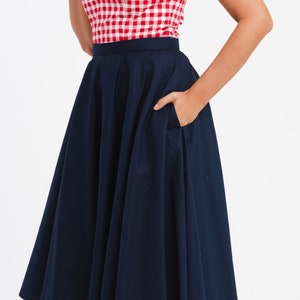 May include: A red and white checkered top with a navy blue skirt. The skirt is a full, flared style with a pocket. The top has a square neckline and white buttons. The outfit is a classic, retro style.