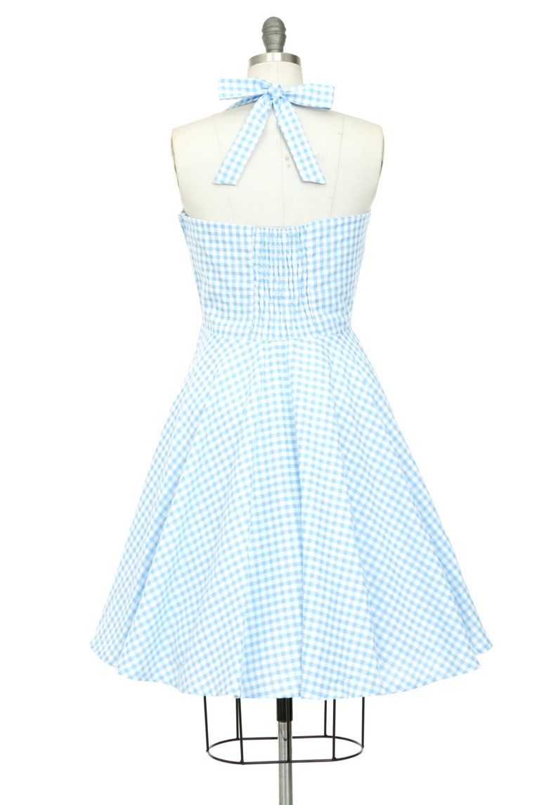 K&ouml;nnte beinhalten: Hellblau-wei&szlig;es Gingham-Halterkleid auf einer Schaufensterpuppe. Das Kleid hat ein figurbetontes Oberteil, einen ausgestellten Rock und eine passende Schleife am Halter-Ausschnitt. Ein klassischer Stil, perfekt f&uuml;r einen Sommertag.