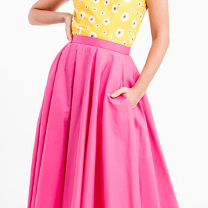 Puede incluir: Una blusa amarilla brillante con estampado de margaritas combinada con una falda rosa vibrante. La falda tiene una cintura ancha y una forma amplia y fluida. El conjunto es alegre y femenino.